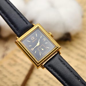 May include: A vintage Seiko watch with a rectangular gold-tone case and a black dial. The watch features gold hands and hour markers, and a small seconds subdial. It has a black leather strap.