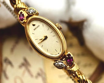 Klasyczny damski zegarek kwarcowy Seiko z lat 90. w kolorze złotym, z owalną tarczą i rubinowym akcentem na łańcuszku