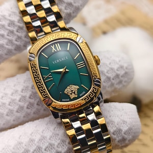 Puede incluir: Reloj Versace dorado y plateado con esfera verde. El reloj presenta n&uacute;meros romanos, agujas doradas y el logotipo de Versace. La correa es una combinaci&oacute;n de eslabones dorados y plateados.