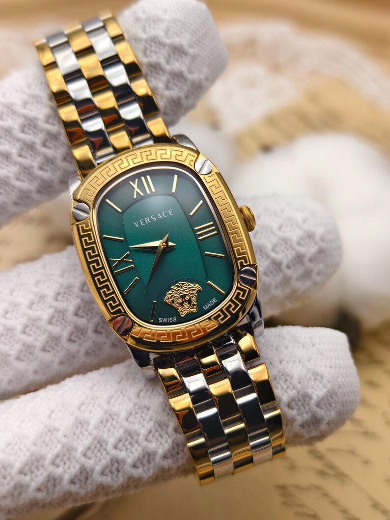 Puede incluir: Reloj Versace dorado y plateado con esfera verde. El reloj presenta n&uacute;meros romanos, agujas doradas y el logotipo de Versace. La correa es una combinaci&oacute;n de eslabones dorados y plateados.