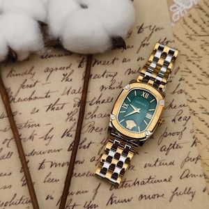Puede incluir: Un reloj Versace dorado y plateado con esfera verde. El reloj tiene una esfera rectangular con n&uacute;meros romanos y el logotipo de Versace. La correa es una mezcla de eslabones dorados y plateados. Sobre un fondo de papel vintage.