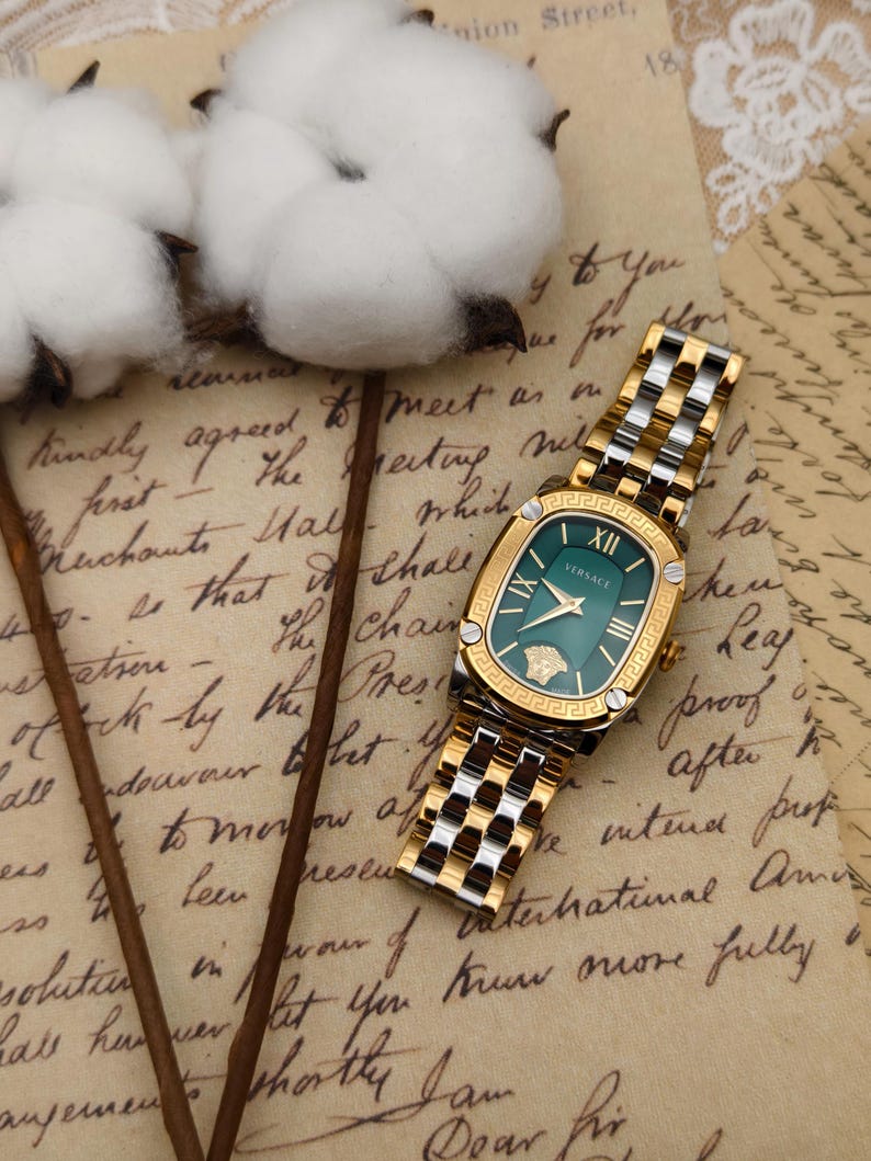Puede incluir: Un reloj Versace dorado y plateado con esfera verde. El reloj tiene una esfera rectangular con n&uacute;meros romanos y el logotipo de Versace. La correa es una mezcla de eslabones dorados y plateados. Sobre un fondo de papel vintage.