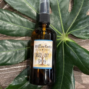 May include: A brown glass bottle with a black spray top and a white label that reads "Willow Roots Essentials Buzz Off Spray 4 oz".
