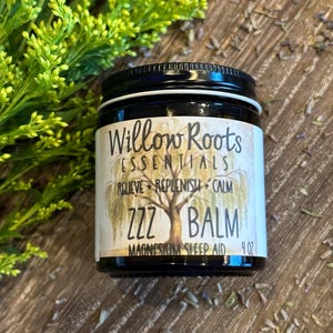 May include: A small glass jar with a black lid and a white label that reads "Willow Roots Essentials, Relieve + Replenish + Calm, ZZZ Balm, Magnesium Sleep Aid, 4 oz."