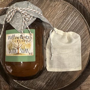 May include: A jar of Willow Roots Essentials Detox Soak, 16 oz, with a fabric lid tied with twine, next to a small, white muslin bag. The jar and bag sit on a wooden tray.