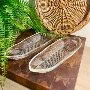 May include: Two clear glass corn on the cob dishes. The dishes are shaped like corn on the cob and have a textured surface.