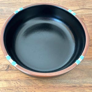 May include: A black ceramic bowl with a brown rim and a blue and white stripe design.