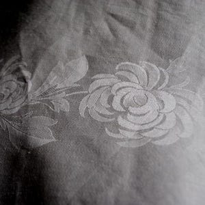 Puede incluir: Un mantel blanco con un patrón floral. El patrón presenta un diseño repetitivo de rosas estilizadas con una textura en relieve.