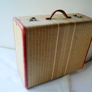 May include: A vintage striped suitcase with a brown and tan striped pattern and a red leather trim. The suitcase has a brown leather handle.