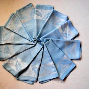 May include: A set of twelve blue linen napkins with a white floral design. The napkins are folded and arranged in a circle.