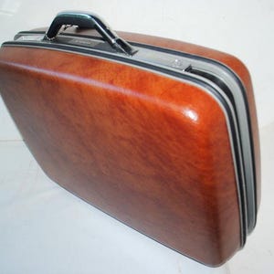 May include: A brown hard-sided suitcase with a silver handle and trim. The suitcase has a wood-grain pattern.