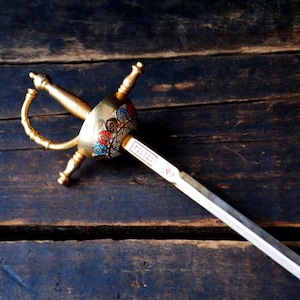 Puede incluir: Una espada decorativa dorada con un mango detallado sobre un fondo de madera oscura.