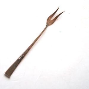 May include: A vintage silver-toned serving fork with two tines. The handle has a rectangular shape with a decorative floral design. The fork is angled against a white background.