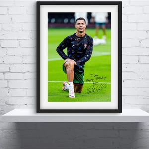 May include: A framed photo of a soccer player wearing a black and green jersey with a white signature below the image. The signature reads "To you Happy Birthday from CR7".