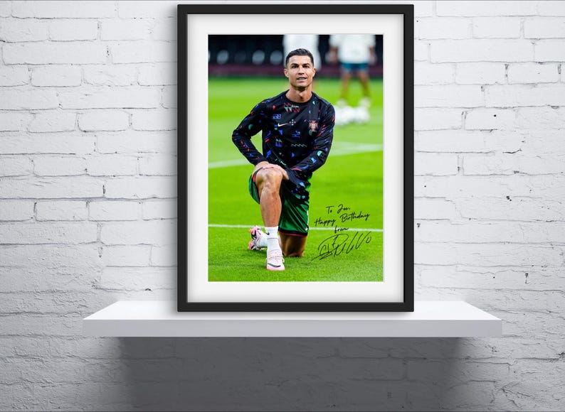 May include: A framed photo of a soccer player wearing a black and green jersey with a white signature below the image. The signature reads "To you Happy Birthday from CR7".