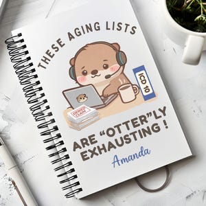 May include: A white spiral-bound notebook featuring a cartoon otter wearing a headset, working on a laptop next to a mug and a stack of papers labeled DENIED CLAIM. The text reads THESE AGING LISTS ARE OTTERLY EXHAUSTING and the name Amanda.
