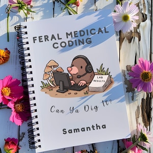 May include: A spiral-bound notebook with a white cover featuring a cartoon mole wearing a headset at a computer. The text reads FERAL MEDICAL CODING, LAB RESULTS, Can Ya Dig It?, and Samantha. The design includes mushrooms and grass.