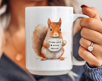 May include: White ceramic mug with a watercolor illustration of a squirrel holding a mug that says "bright eyed & bushy tailed!"