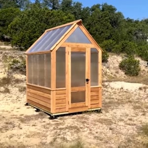 Puede incluir: Un pequeño invernadero de madera con techo y paredes de plástico transparente. El invernadero está situado en un suelo de tierra.