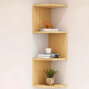 May include: A three-tiered corner shelf unit made of light wood. The shelves are curved and have a staggered design. The top shelf has a small orange animal figurine and two books. The middle shelf has a white mug and two books. The bottom shelf has a small potted plant.