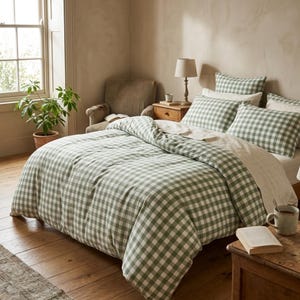 May include: A bed with a green and white gingham patterned duvet cover and matching pillowcases. The bedroom has a wooden floor, a window, a potted plant, and a small wooden side table with a lamp.