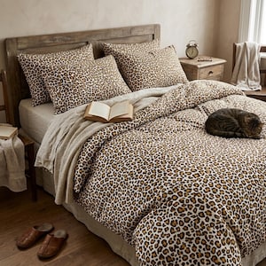 May include: A bed featuring a duvet cover and two pillowcases with a brown, black, and tan leopard print pattern. A beige throw blanket is draped across the bed, and an open book rests on the surface. A tabby cat is curled up on the duvet.