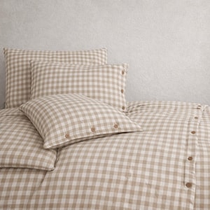May include: A beige and white gingham bedding set. The set includes a duvet cover and several pillows. The pillows have button closures. The bedding is arranged on a bed. The fabric has a soft, textured appearance.