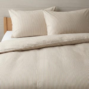 May include: A bedding set featuring a duvet cover and two rectangular pillowcases, all decorated with a consistent pattern of thin, vertical beige and white stripes. The fabric appears smooth and covers a bed frame with a light wood headboard.