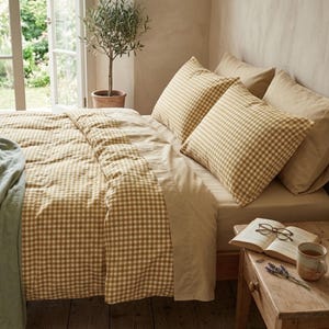 Peut inclure: Un lit avec une housse de couette et deux taies d'oreiller à motif vichy jaune moutarde et blanc. L'ensemble de literie est complété par des taies d'oreiller beige uni et un drap plat, créant un aspect coordonné pour une chambre à coucher.