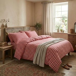 Pode incluir: Um quarto com uma cama vestida com um conjunto de edredão xadrez vermelho e branco. Uma manta cinzenta é colocada aos pés da cama. O quarto tem um estilo rústico, com mobiliário em madeira e uma janela.