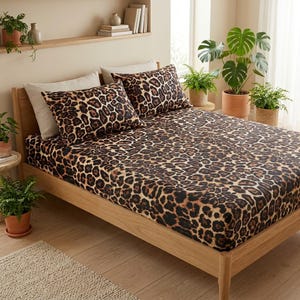 May include: A bed featuring a fitted sheet and two pillowcases with a brown and black leopard print pattern. The bedding set is displayed on a light-colored wooden bed frame, paired with two solid off-white rectangular pillows.