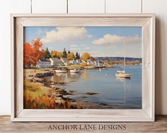 May include: A framed painting of a coastal town with white houses, fall foliage, and a sailboat on the water. The painting is in a light wood frame and has the text "ANCHOR LANE DESIGNS" at the bottom.