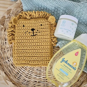May include: A wicker basket filled with baby care items, including a crocheted lion washcloth, a jar of baby bum butter, and a bottle of Johnson's head-to-toe wash and shampoo.
