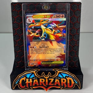 May include: A Mega Charizard Y trading card encased in a clear magnetic protective holder, displayed on a black stand with a red honeycomb pattern and the word CHARIZARD in stylized orange and blue lettering at the base.