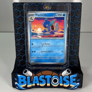 Puede incluir: Una carta coleccionable de Pokemon Wartortle en una funda protectora transparente, montada en un soporte negro con el logotipo de Blastoise en azul y beige en la base. El soporte presenta un patr&oacute;n de panal negro en el panel trasero.