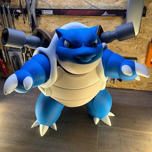 May include: A large, blue and white Blastoise figure, a popular character from the Pokémon franchise. The figure has a detailed design, with its signature cannons on its back and white spikes on its limbs. The figure is standing on a wooden surface.