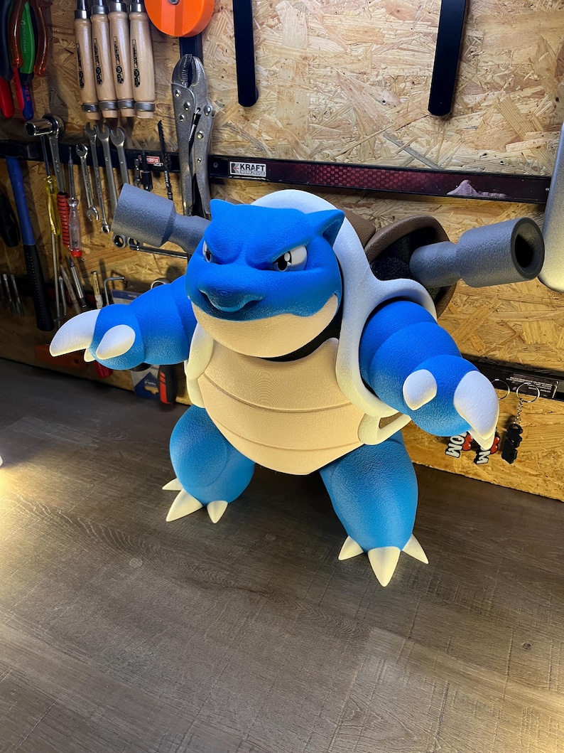 May include: A blue and white Blastoise figure, a popular character from the Pok&eacute;mon franchise. The figure has a light tan shell, blue body, and two gray cannons on its back. The figure is standing on a wooden surface.