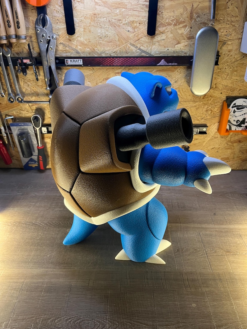 May include: A blue and brown Blastoise figure, a popular character from the Pok&eacute;mon franchise. The figure has a brown shell, two black cannons, and white accents. The figure is standing on a wooden surface.