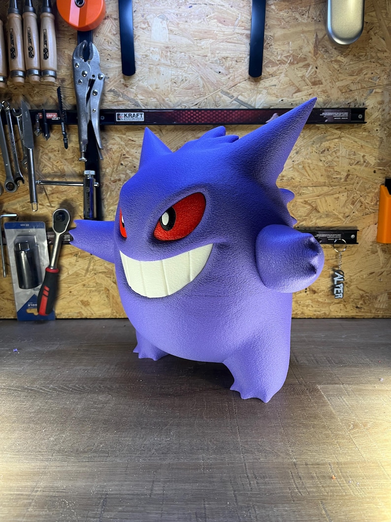 May include: A 3D-printed purple Gengar figure with a wide grin, red eyes, and spiky features. The figure is standing on a wooden surface. The figure is a popular character from the Pokemon franchise.