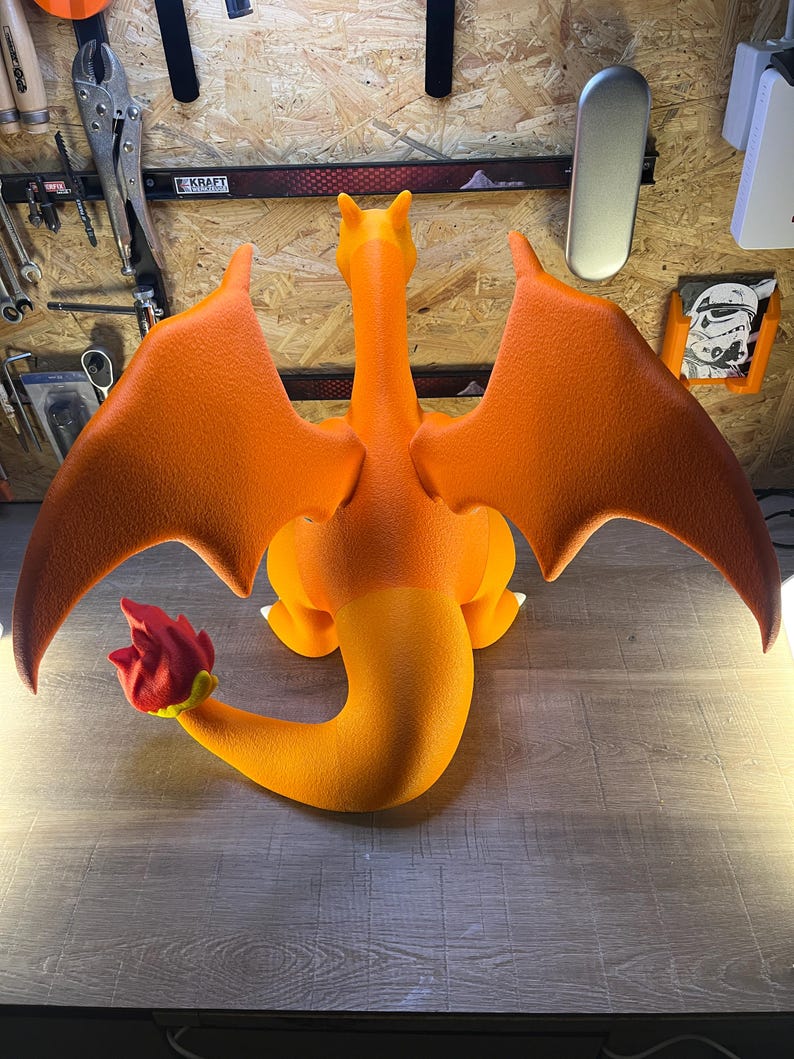 May include: An orange and yellow Charizard figure with outstretched wings and a fiery tail. The figure is posed on a wooden surface, showcasing its detailed design and vibrant colors. The figure is a popular character from the Pokemon franchise.