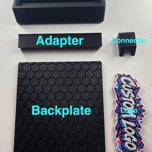 K&ouml;nnte beinhalten: Ein Set aus schwarzen 3D-gedruckten Komponenten mit den Beschriftungen Part Description, Base, Adapter, Connector und Backplate. Die R&uuml;ckplatte hat ein Sechseckmuster. Ein Aufkleber mit dem Text Custom Logo ist enthalten.