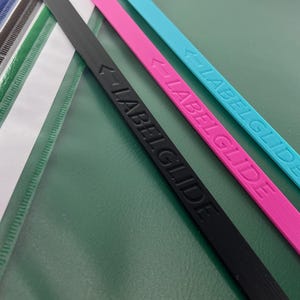 Peut inclure: Une collection de bandes en plastique fines, plates et rectangulaires de diff&eacute;rentes couleurs, dont jaune, bleu, noir, blanc, vert, rose et cyan. Les bandes noire, rose et cyan portent le texte en relief LABELGLIDE avec une ic&ocirc;ne de fl&egrave;che.