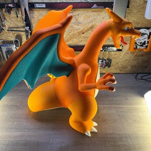 May include: An orange and teal Charizard figure, a popular character from the Pok&eacute;mon franchise. The figure is posed in a dynamic stance, with its wings spread and claws extended. The figure is made of a textured material.