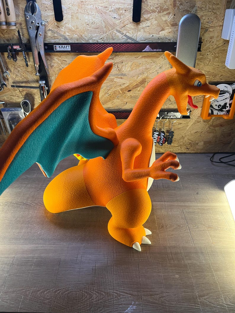 May include: An orange and teal Charizard figure, a popular character from the Pok&eacute;mon franchise. The figure is posed in a dynamic stance, with its wings spread and claws extended. The figure is made of a textured material.