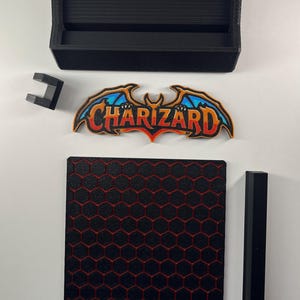 May include: A black rectangular box, a small black bracket, a black vertical bar, and a square base with a red honeycomb pattern. A colorful emblem features the text Charizard in orange and yellow with blue wings and a black outline.