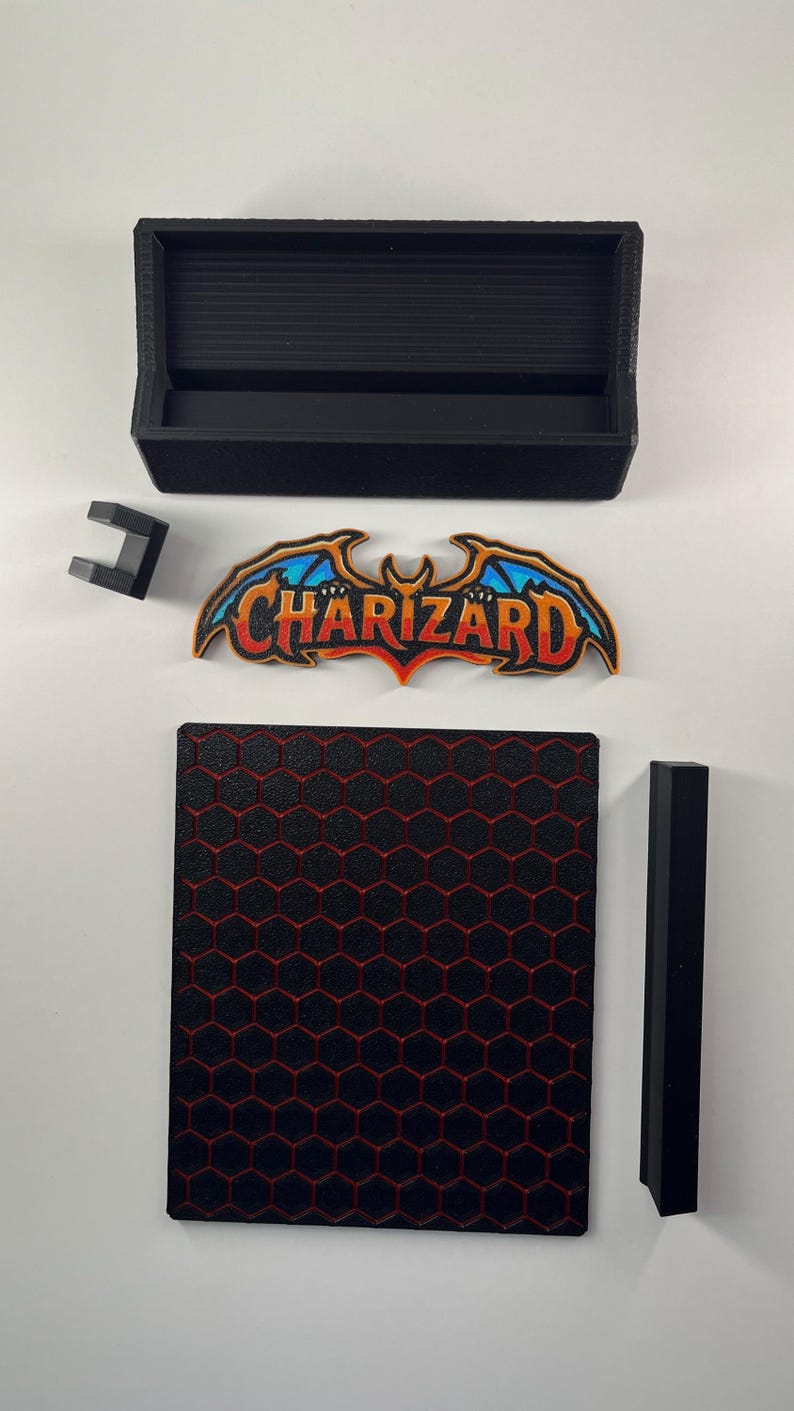 May include: A black rectangular box, a small black bracket, a black vertical bar, and a square base with a red honeycomb pattern. A colorful emblem features the text Charizard in orange and yellow with blue wings and a black outline.