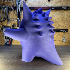 May include: A purple 3D-printed sculpture of a creature with a textured surface and spiky details. The artwork is set against a wooden background with tools visible. The sculpture is a gradient of purple.