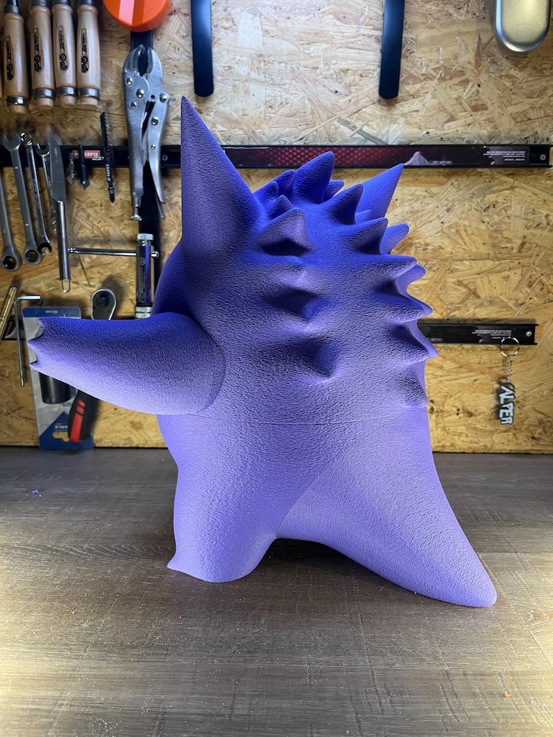 May include: A purple 3D-printed sculpture of a creature with a textured surface and spiky details. The artwork is set against a wooden background with tools visible. The sculpture is a gradient of purple.