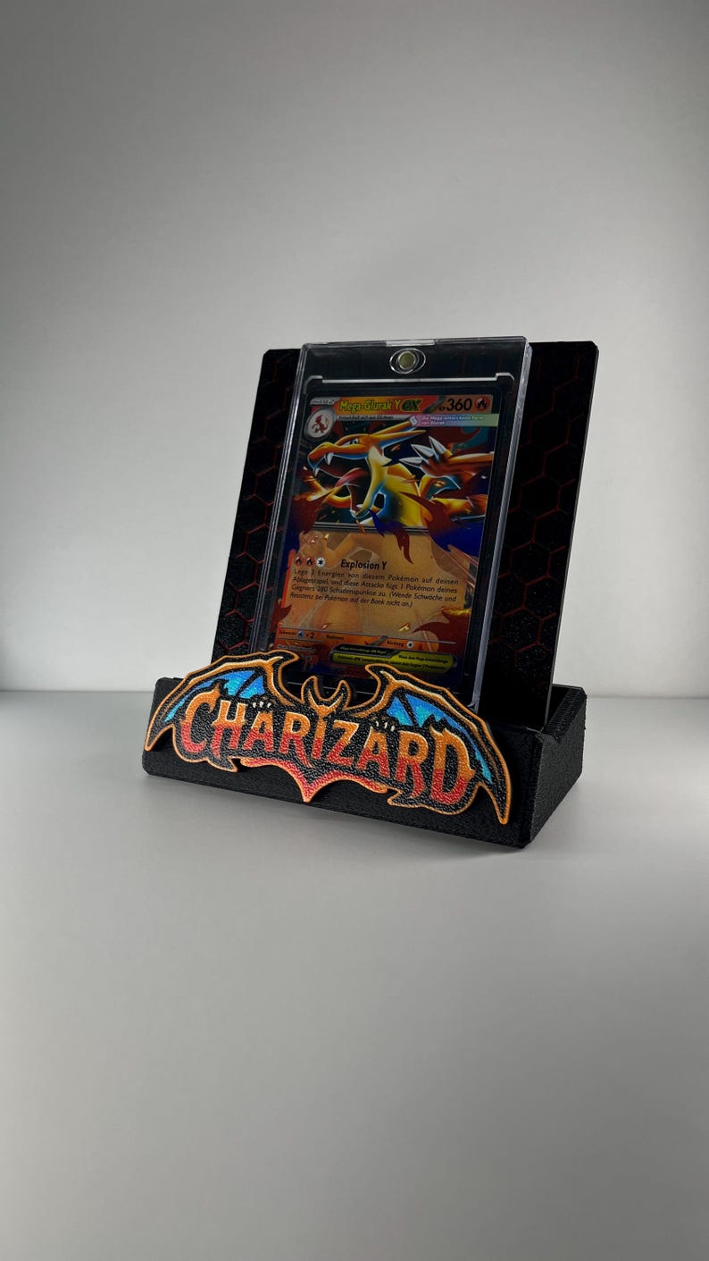 May include: A black display stand featuring a prominent Charizard logo with blue and orange wings. The stand holds a Mega Charizard Y EX trading card encased in a clear protective magnetic holder, set against a black hexagonal patterned backplate.