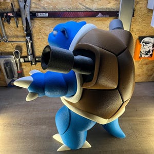 May include: A blue and brown Blastoise figurine, a Pok&eacute;mon character, is displayed in profile. The figurine features a blue body, a brown shell, and white accents. The figure has two cannons extending from its shell.